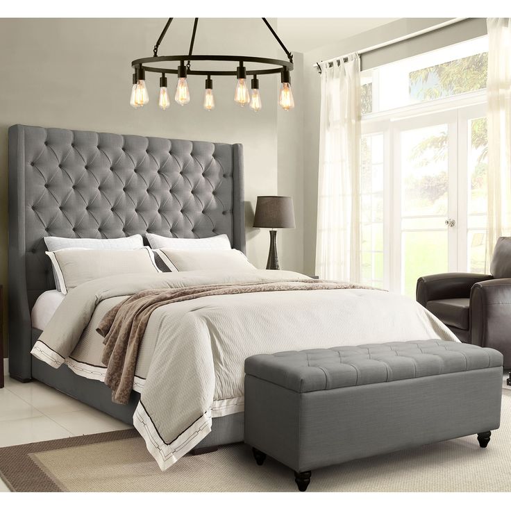 a bedroom with a large bed, chair and ottoman in grey fabric on the floor