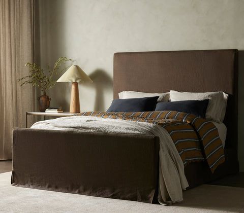 a bed with green headboard and pillows in a room next to a lamp on a table