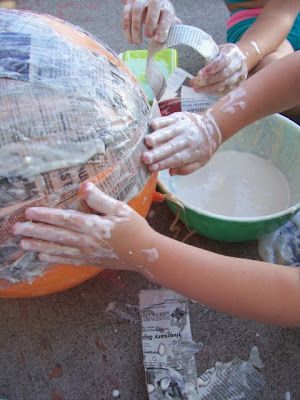 two children are washing their hands on an orange ball with newspaper pages all over it