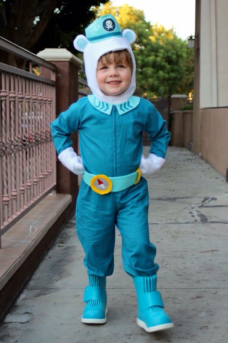 a little boy in a blue costume standing on the sidewalk with his hands in his pockets