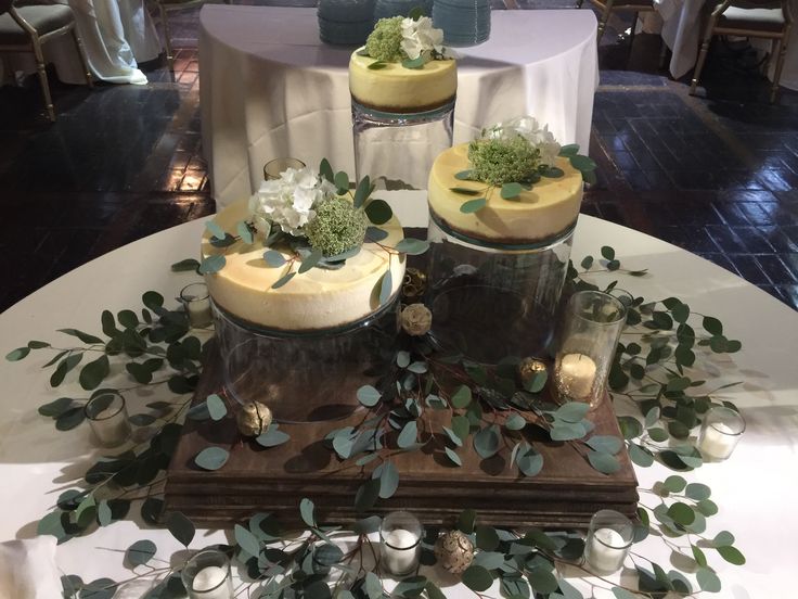 there are two cakes on the table with flowers and greenery around them at this wedding reception