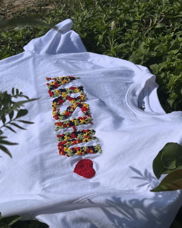 a white t - shirt with the word love spelled out in flowers and beads on it