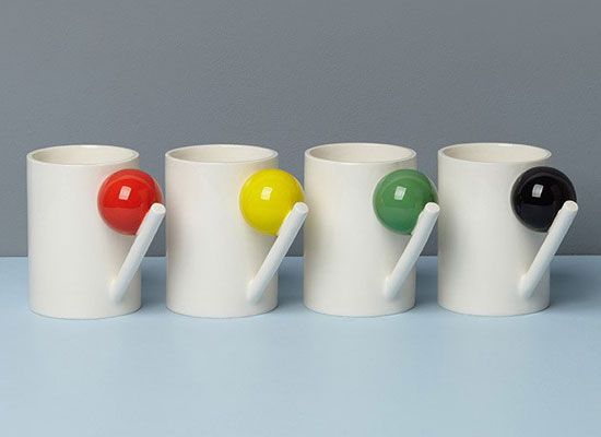 four coffee mugs with different colored balls in the middle one has a spoon and two are empty