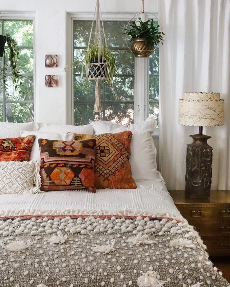 a bed with lots of pillows on top of it next to two lamps and windows