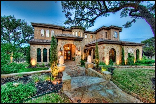 a large house that is in the middle of a field with trees and bushes around it