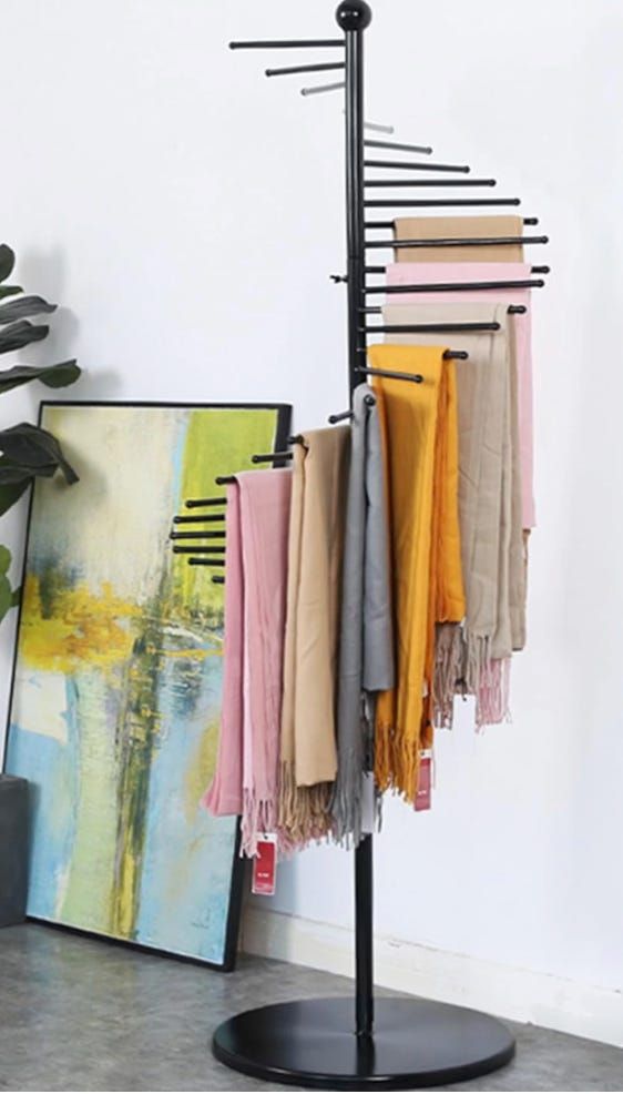 a coat rack with several scarves hanging from it's sides and a potted plant in the background