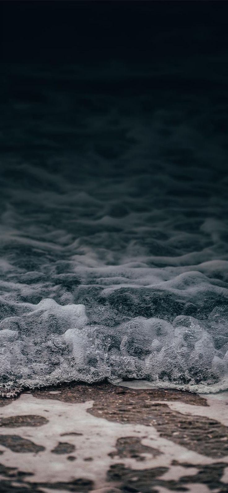 an ocean with waves coming in to shore and dark sky above the water at night