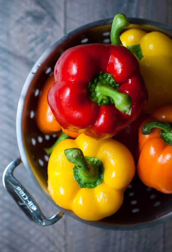 peppers and broccoli in a colander on a wooden table, top view