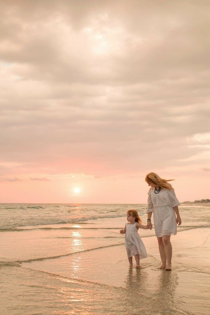 a mother and daughter walking on the beach at sunset