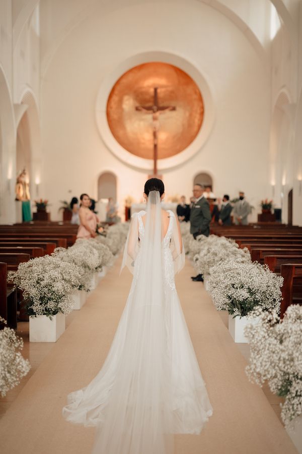 the bride is walking down the aisle in her wedding dress with veil on, and flowers all around