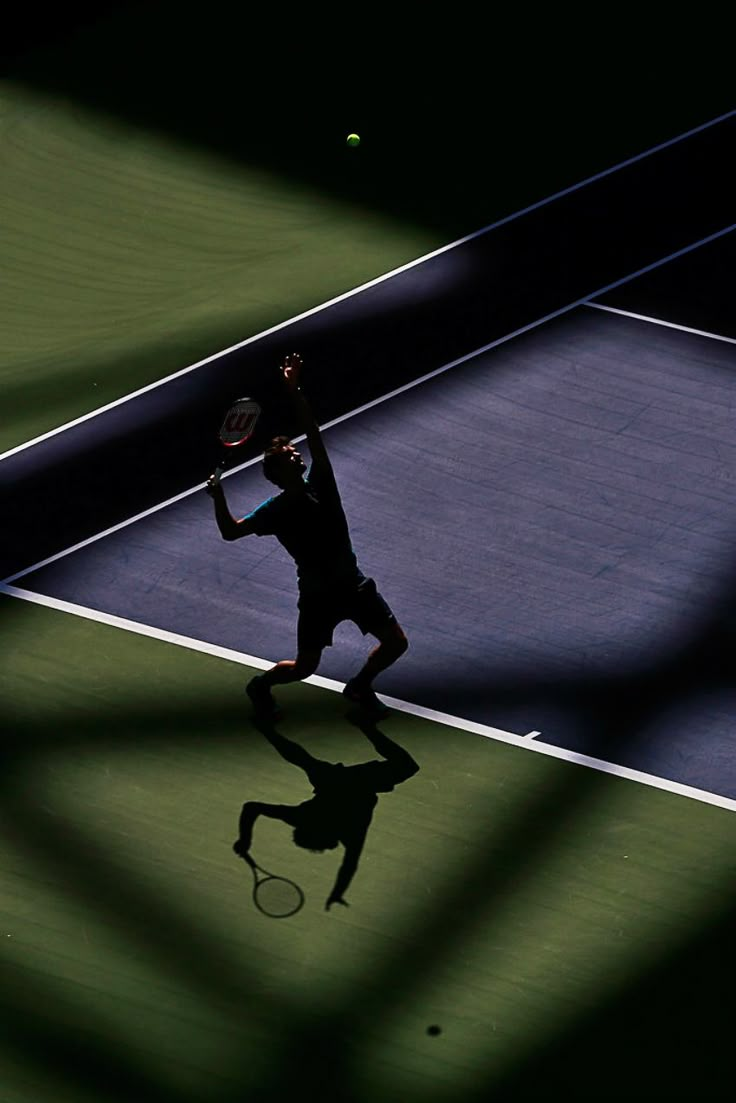 a man holding a tennis racquet on top of a tennis court in the dark