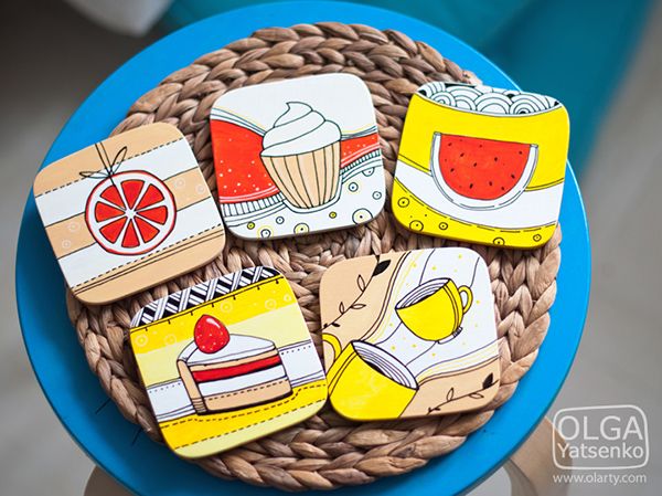 four coasters with pictures of food on them sitting on a blue table top next to a wicker basket