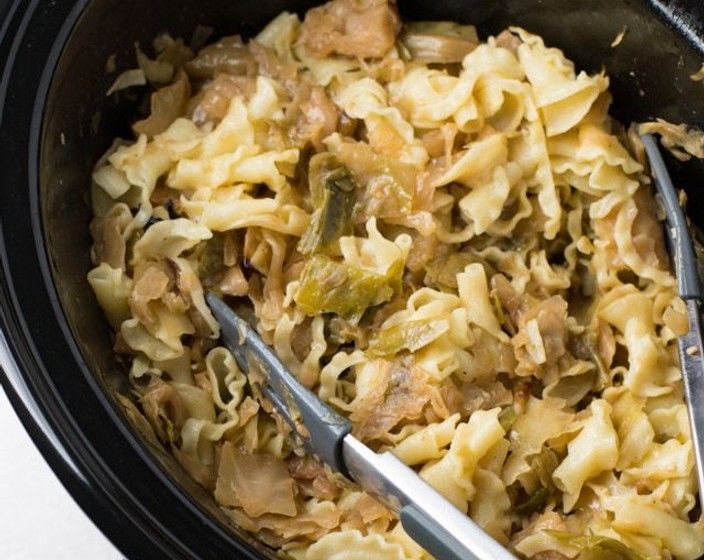 a crock pot filled with pasta and meat next to two tongs in it