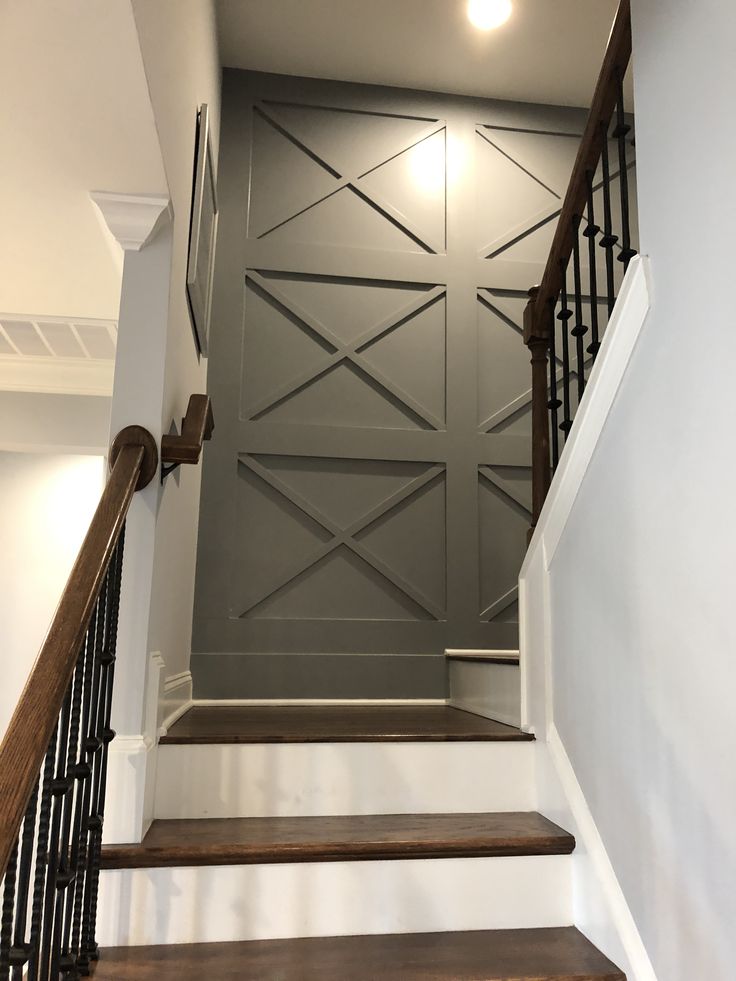 an empty staircase leading up to a gray wall with black railings and wooden handrails