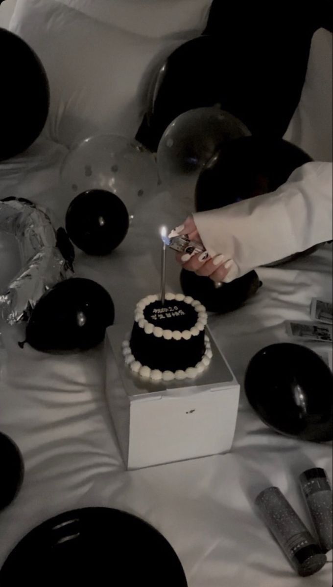 a person lighting a candle on top of a black and white birthday cake with pearls