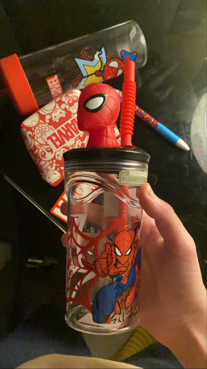 a hand holding a glass cup with spiderman on it and other items in the background