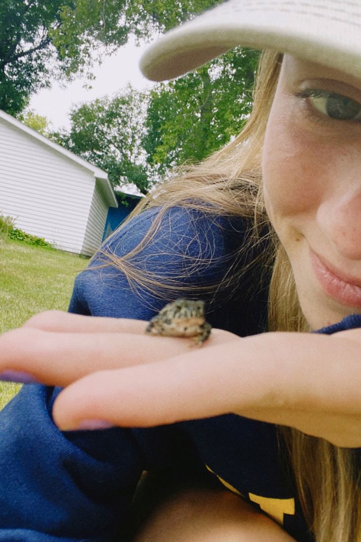 a woman holding a small frog in her hand while wearing a hat and blue shirt