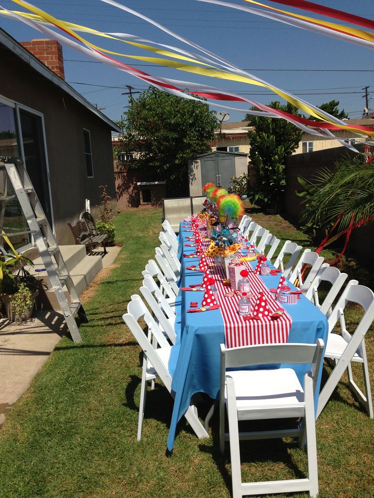 a long table is set up outside in the yard for an outdoor party with balloons and streamers