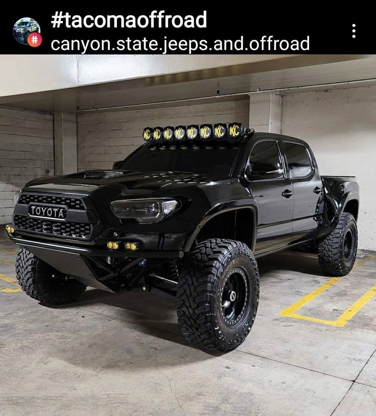 a large black truck parked in a parking garage next to a wall with the words tacomaofroad written on it