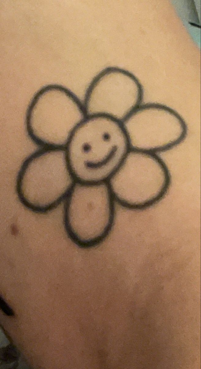 a smiley face flower tattoo on the back of a woman's left shoulder,