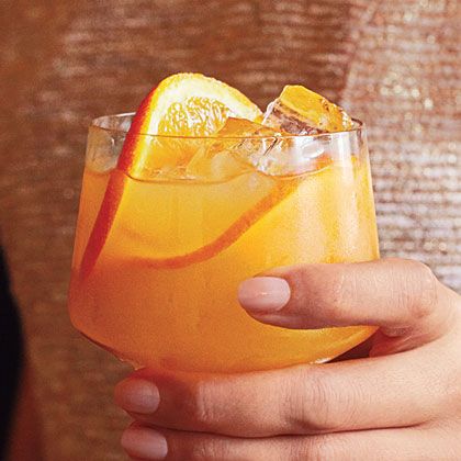 a woman is holding a glass with orange juice and an orange slice on the rim