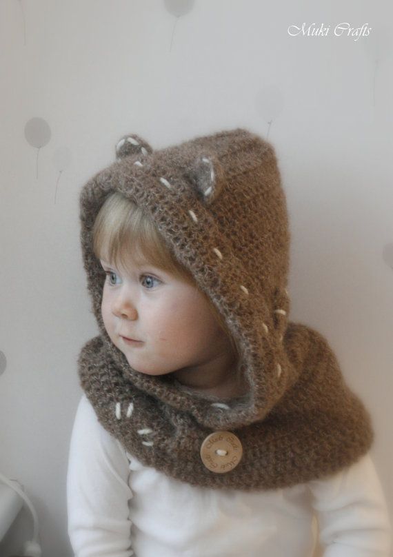 a young child wearing a knitted bear hat and scarf with buttons on the hood