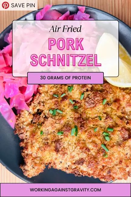 an air fried pork schnitzel on a black plate with pink flowers and lemon wedges