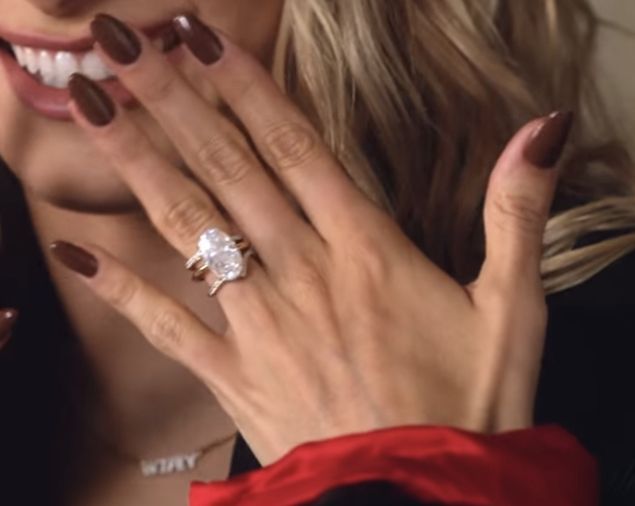 a close up of a person wearing a ring and holding her hands near her face