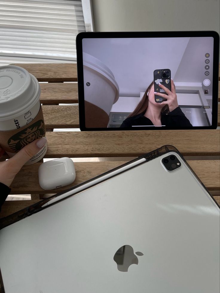 a person taking a photo of an apple laptop with their cell phone and coffee in front of them