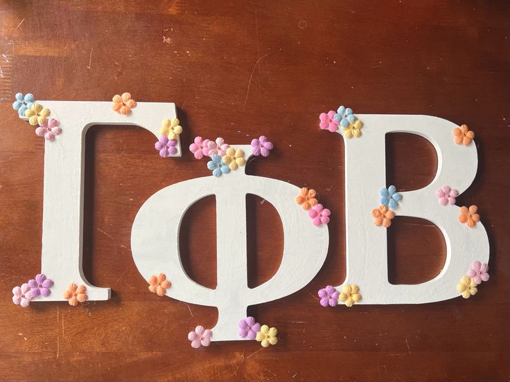 the letters are decorated with small flowers on top of each other and placed in front of a wooden table