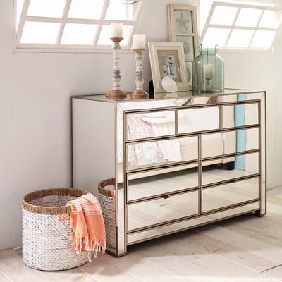 a mirrored dresser with baskets and pictures on the top, next to it is a window