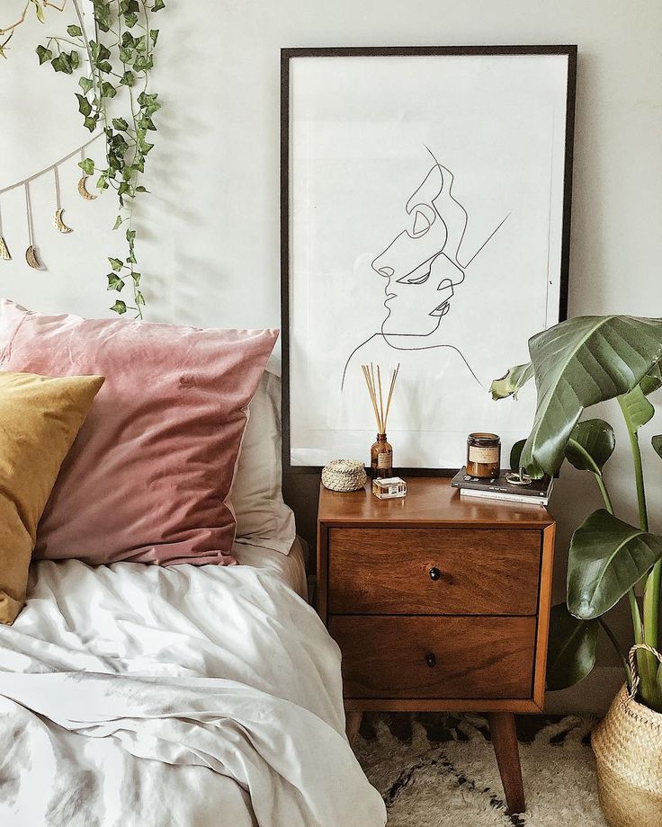 a bed with pillows and plants on top of it next to a framed art piece