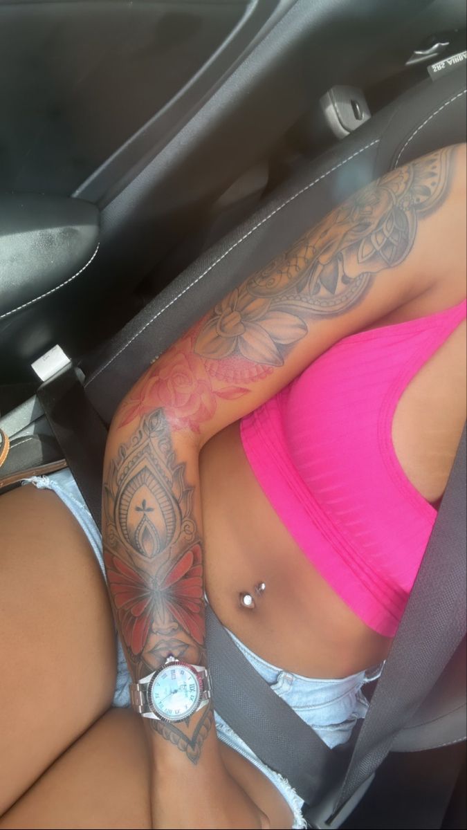 a woman sitting in the back seat of a car with tattoos on her arm and chest