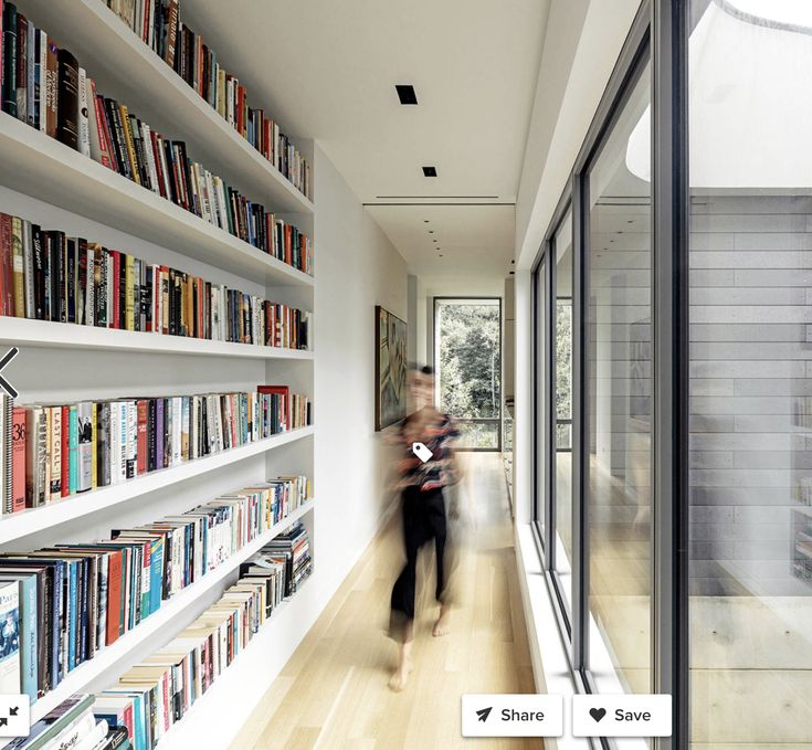 a woman walking down a hallway next to a bookshelf filled with lots of books