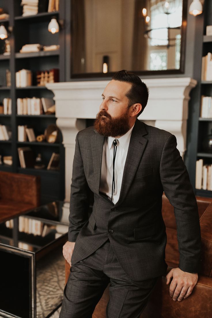 a man in a suit and tie is sitting on a couch with bookshelves behind him