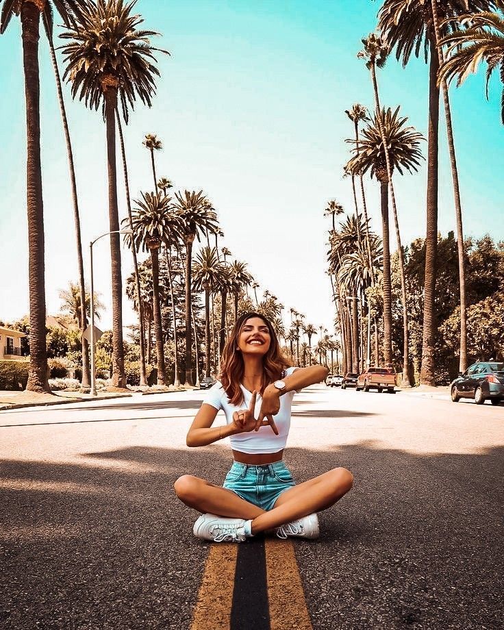 a woman sitting in the middle of a road with palm trees around her and smiling