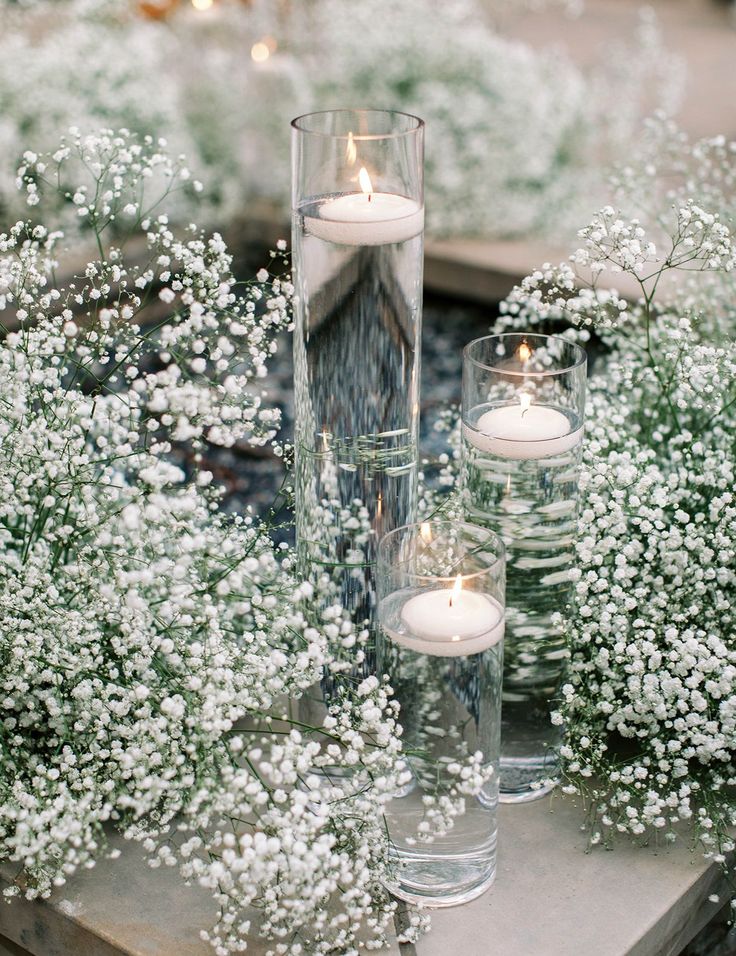 candles are placed in glass vases on a table surrounded by white flowers and baby's breath