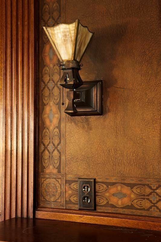 an old fashioned wall light on the side of a wooden shelf in front of a patterned wall