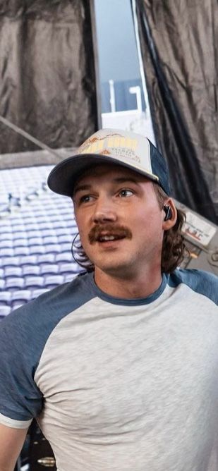 a man with a mustache standing in front of a tent and looking at the camera