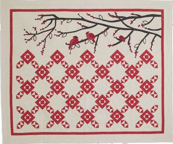 a red and white quilt with two birds on the tree branch in front of it