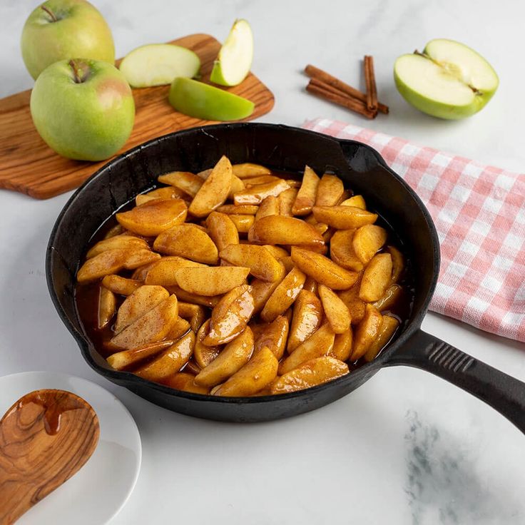 apple slices in a skillet on a counter with apples and cinnamon sticks next to it