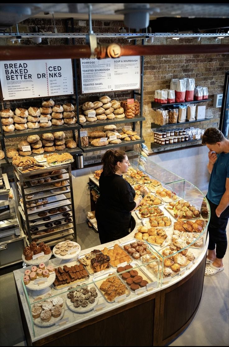 two people standing in front of a counter filled with pastries