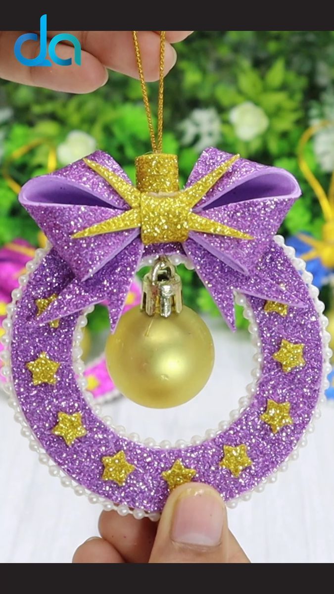 a hand holding a christmas ornament with a purple ribbon and gold bow on it