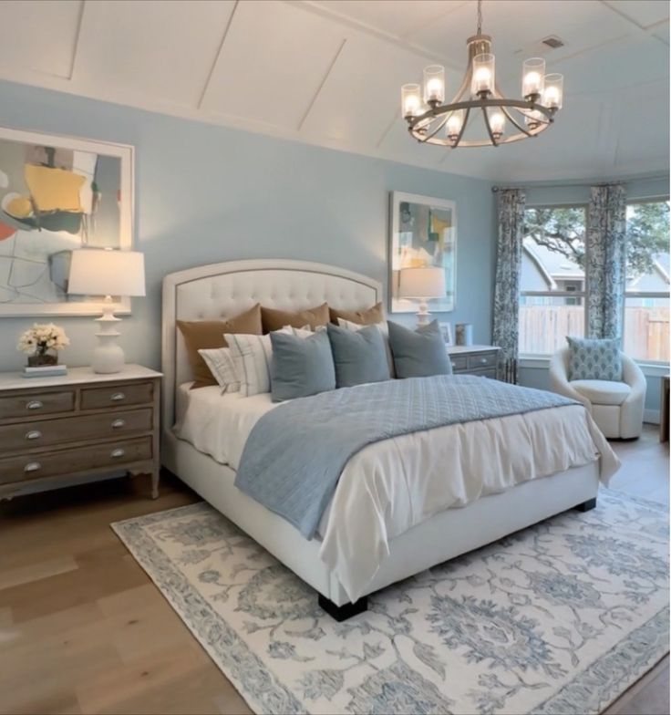 a bedroom with blue walls and white bedding, chandelier, dressers, and windows