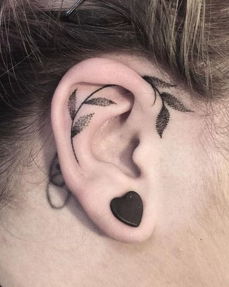 a woman's ear with leaves on it and a black heart behind the ear