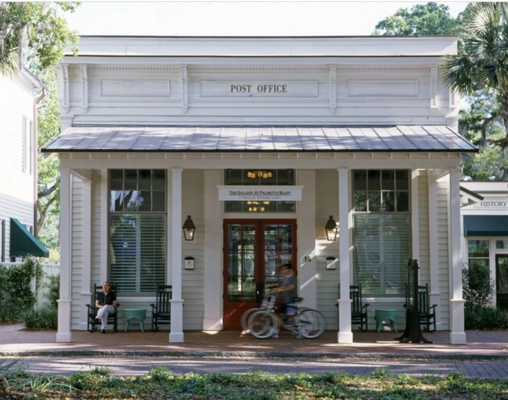 two people sitting on benches in front of a white building with porches and windows