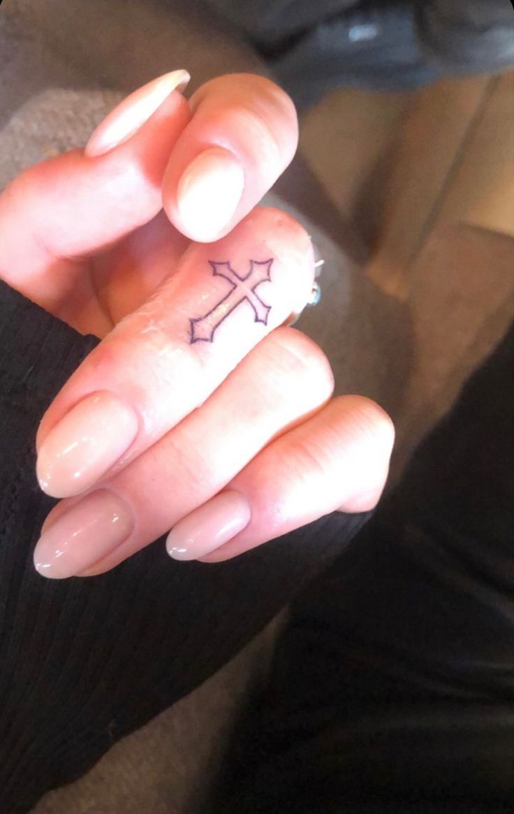 a woman's hand with a small cross tattoo on her thumb and ring finger