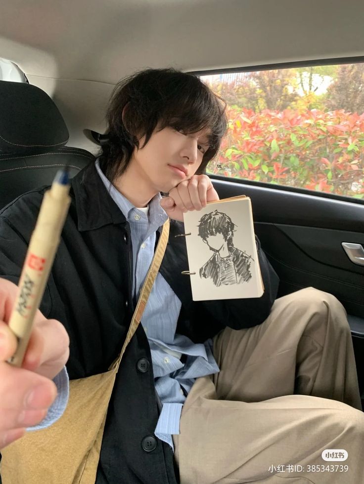 a young man sitting in the back seat of a car holding a pen and paper