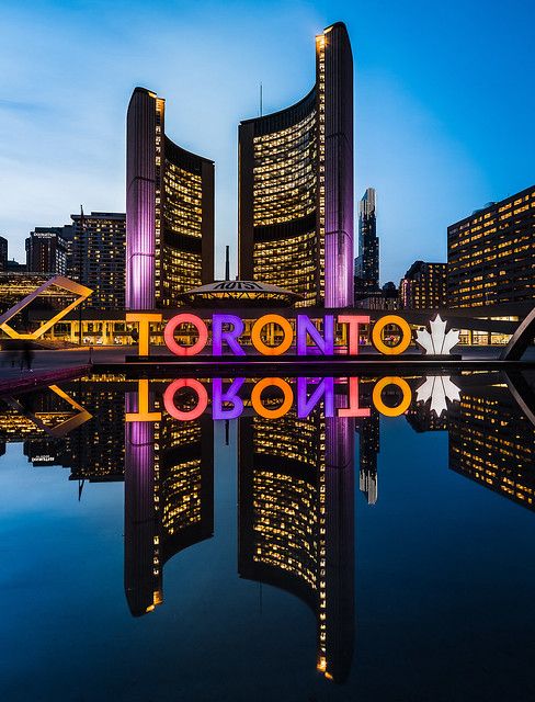 the words toronto are lit up at night in front of skyscrapers and water with reflections