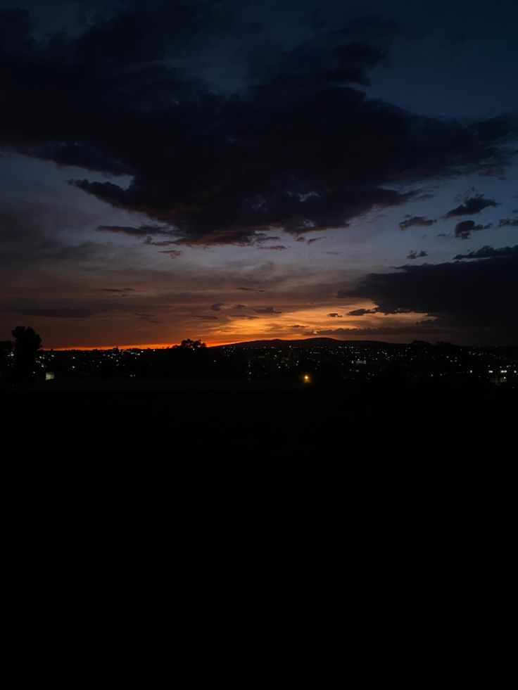 the sun is setting behind some clouds in the sky over a field with trees and buildings